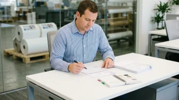 Manufacturing Procurement Specialist Analyzing Purchase Order Manufacturing procurement specialist reviews a purchase order in a modern office with warehouse visibility, demonstrating efficient operations.